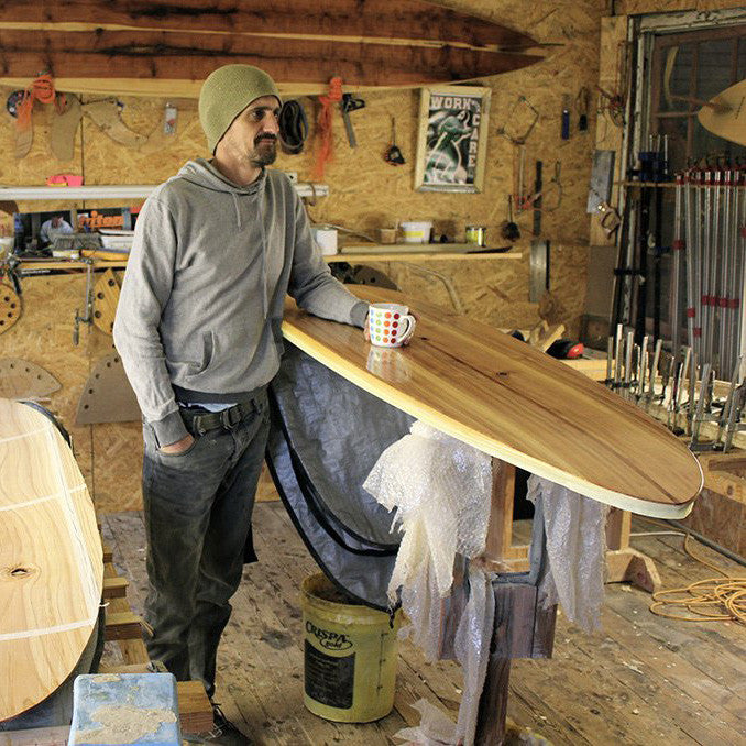 Sealand Gear Ambassador Patrick Burnett Standing Next to wooden surfboard